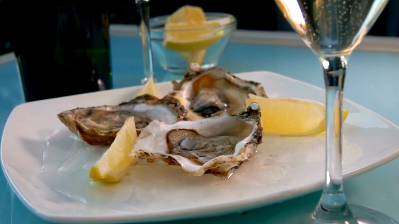 Fresh oysters with lemon wedges on a plate served alongside glasses of sparkling wine
