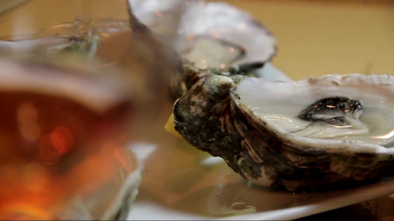 Fresh oysters served on a plate with a drink in the background