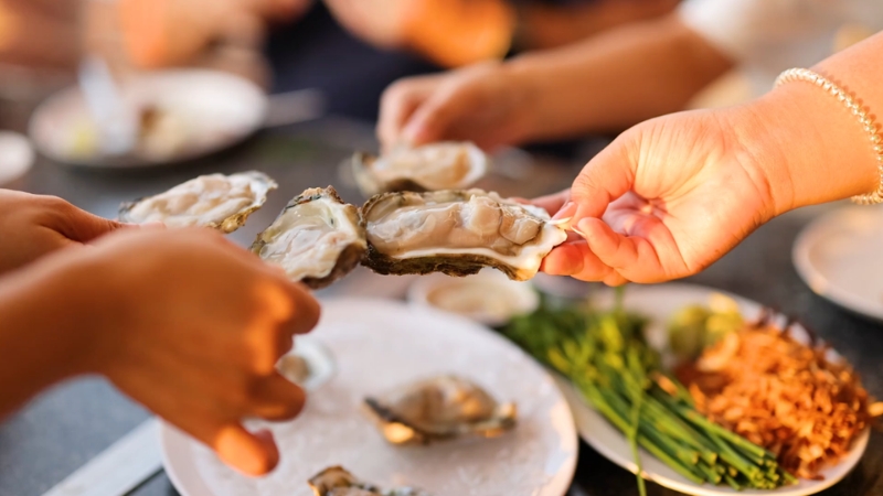 People holding fresh oysters over a table with plates and garnishes in the background