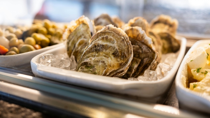 Fresh oysters are stored on ice in a white tray at a seafood counter
