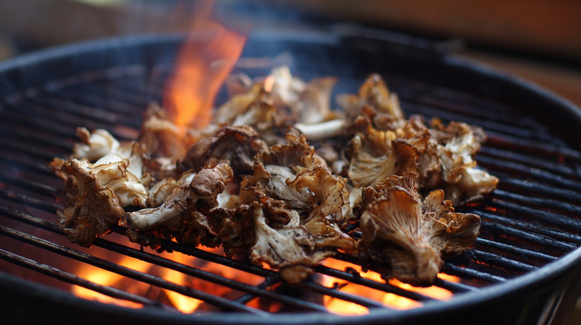 Maitake mushrooms grilling over open flames on a barbecue, developing a smoky char